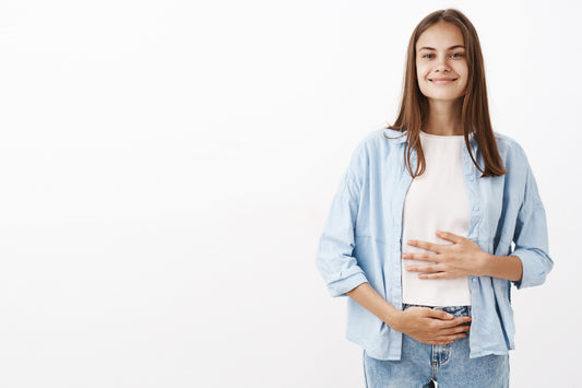 A smiling woman holding her stomach, looking healthy and happy. She has a glowing complexion and a confident expression, indicating her good gut health.